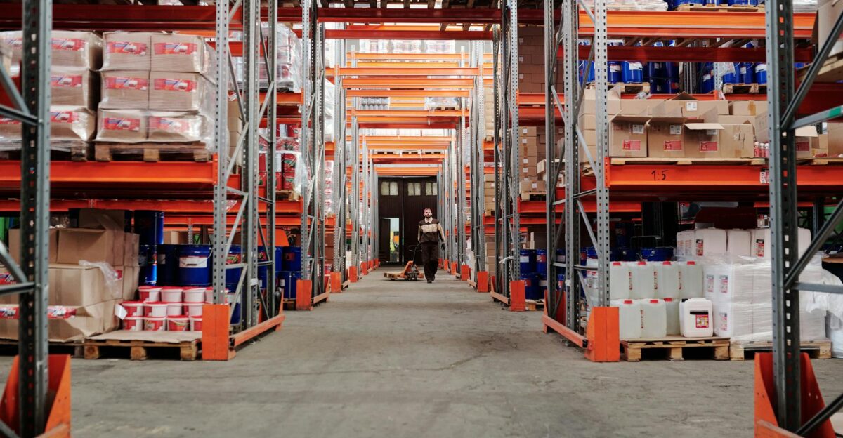 A spacious industrial warehouse with stocked shelves and a worker in protective gear