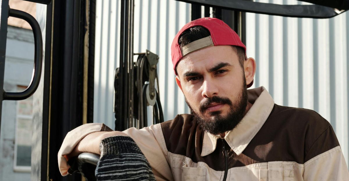 Focused forklift operator in uniform seated in industrial setting, showcasing work environment.
