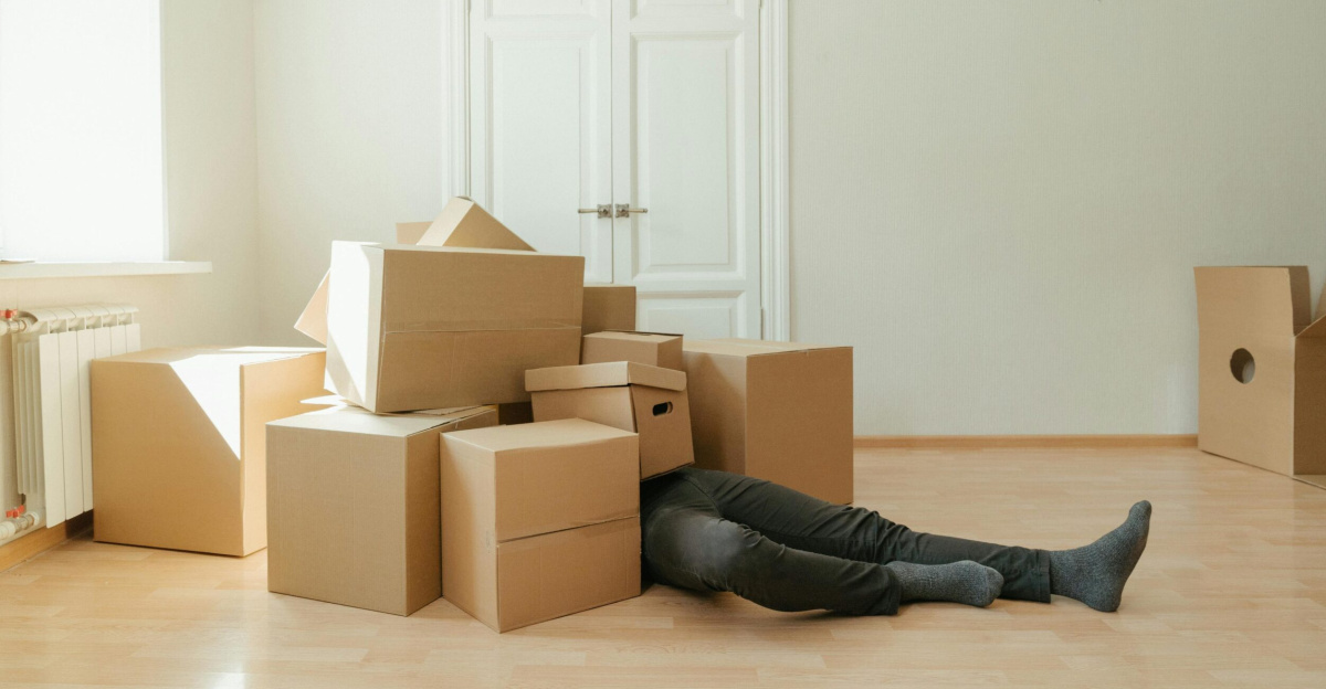 Person on floor surrounded by cardboard boxes during moving; concept of stress and relocation.