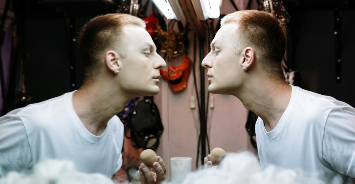 Drag performer applying makeup in a dressing room mirror before a show