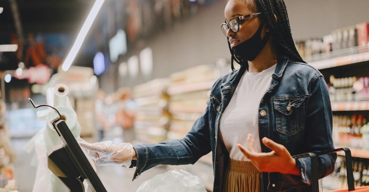 A woman weighing vegetables in a supermarket using a digital scale with a shopping basket.