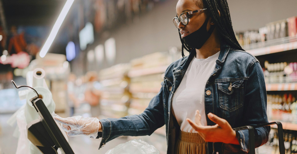 A woman weighing vegetables in a supermarket using a digital scale with a shopping basket.