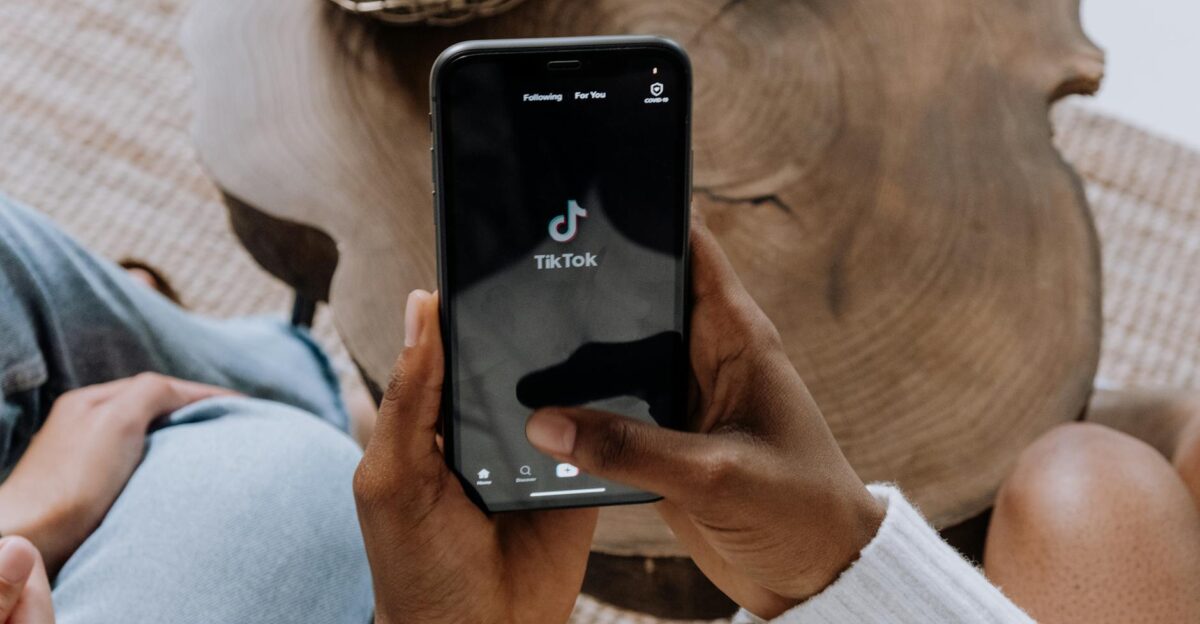 Close-up of hands holding a smartphone displaying the TikTok app interface on a wooden surface