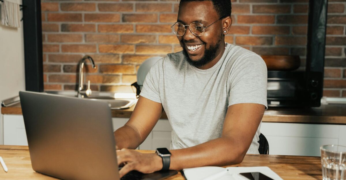 African American man smiling while working remotely on laptop from home office