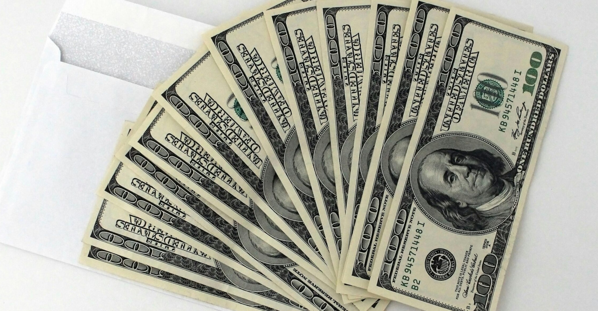 Fan of US $100 bills partially out of a white envelope on a white background.