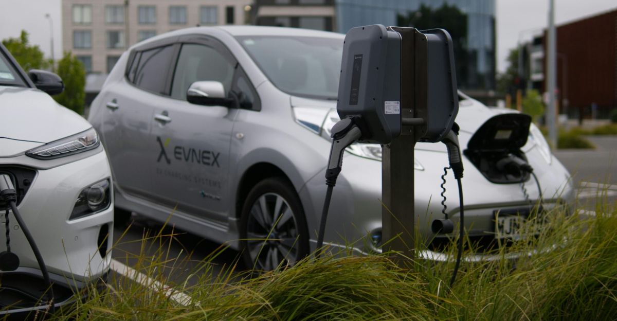 Electric vehicles at a charging station in Christchurch parking lot with modern architecture.