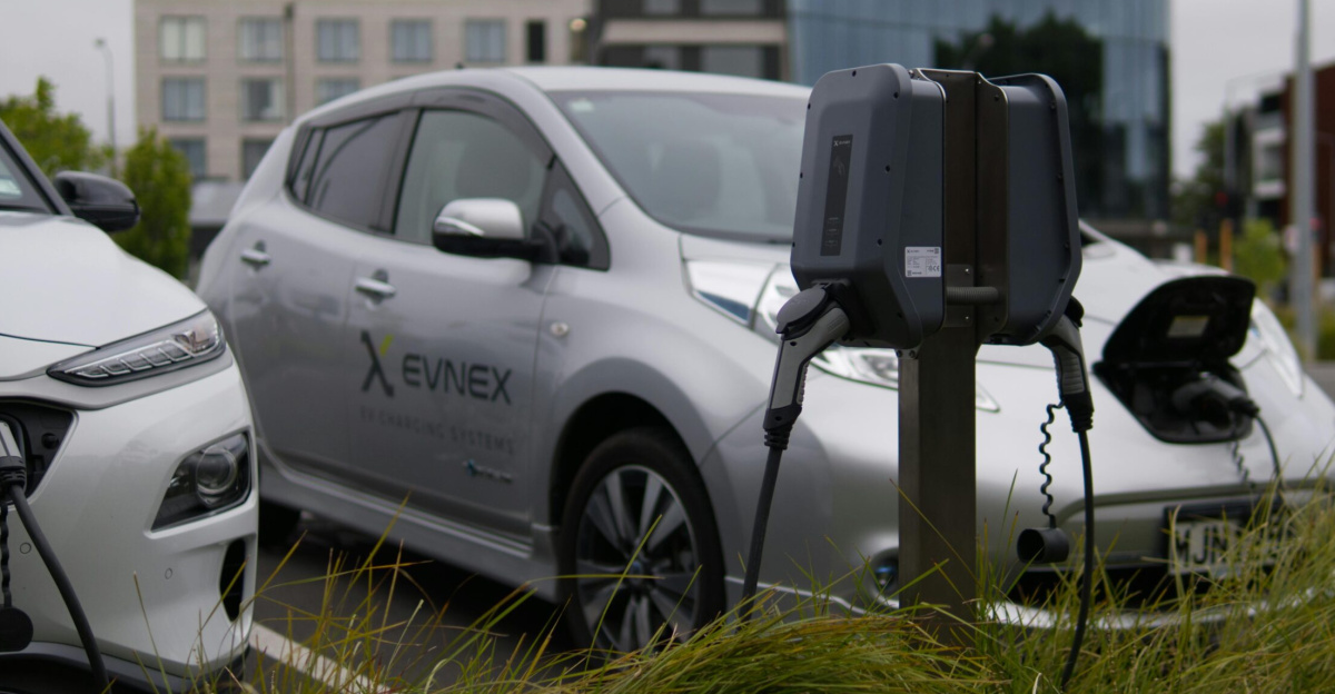 Electric vehicles at a charging station in Christchurch parking lot with modern architecture.
