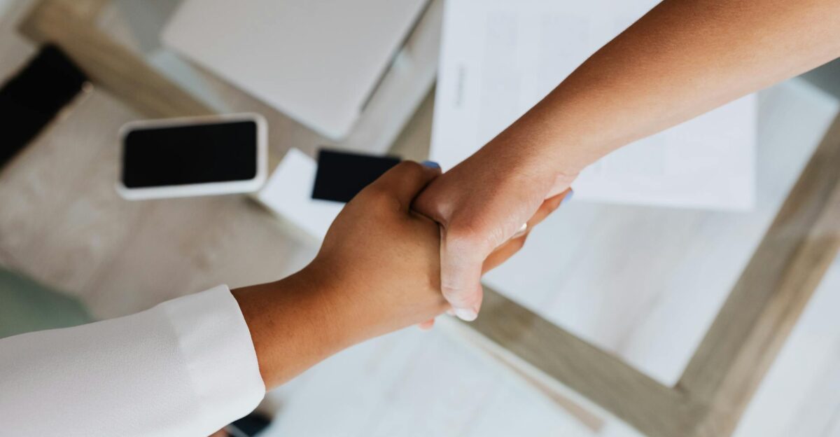 Two people shaking hands over a desk with modern tech symbolizing a successful business agreement