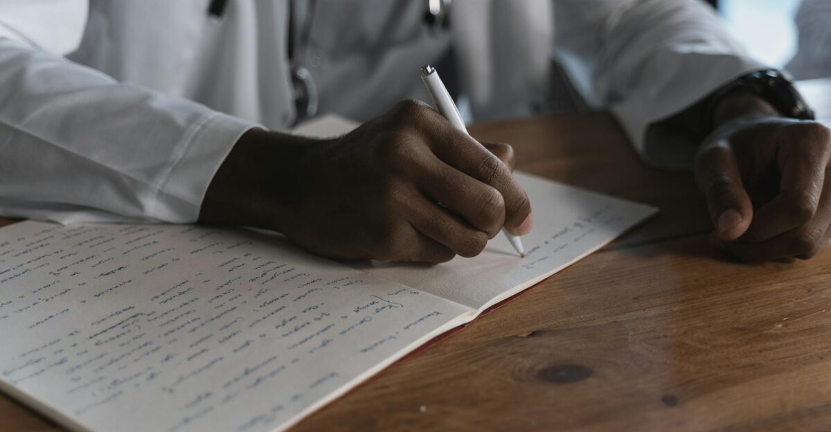 Close-up of a doctor writing notes with a pen in a medical notebook on a wooden desk