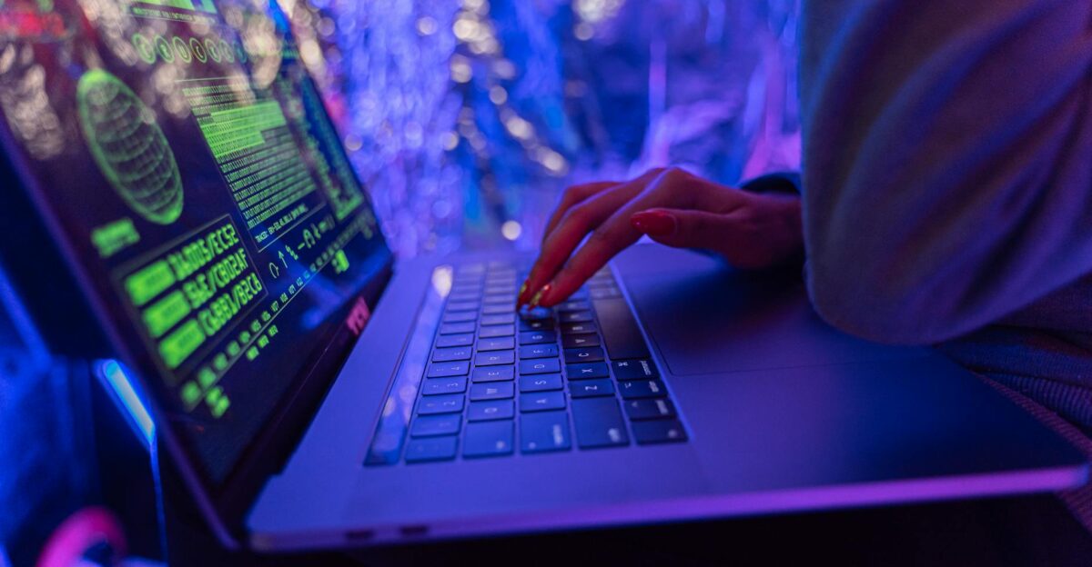 Close-up of hands typing on a laptop displaying cybersecurity graphics illuminated by purple light