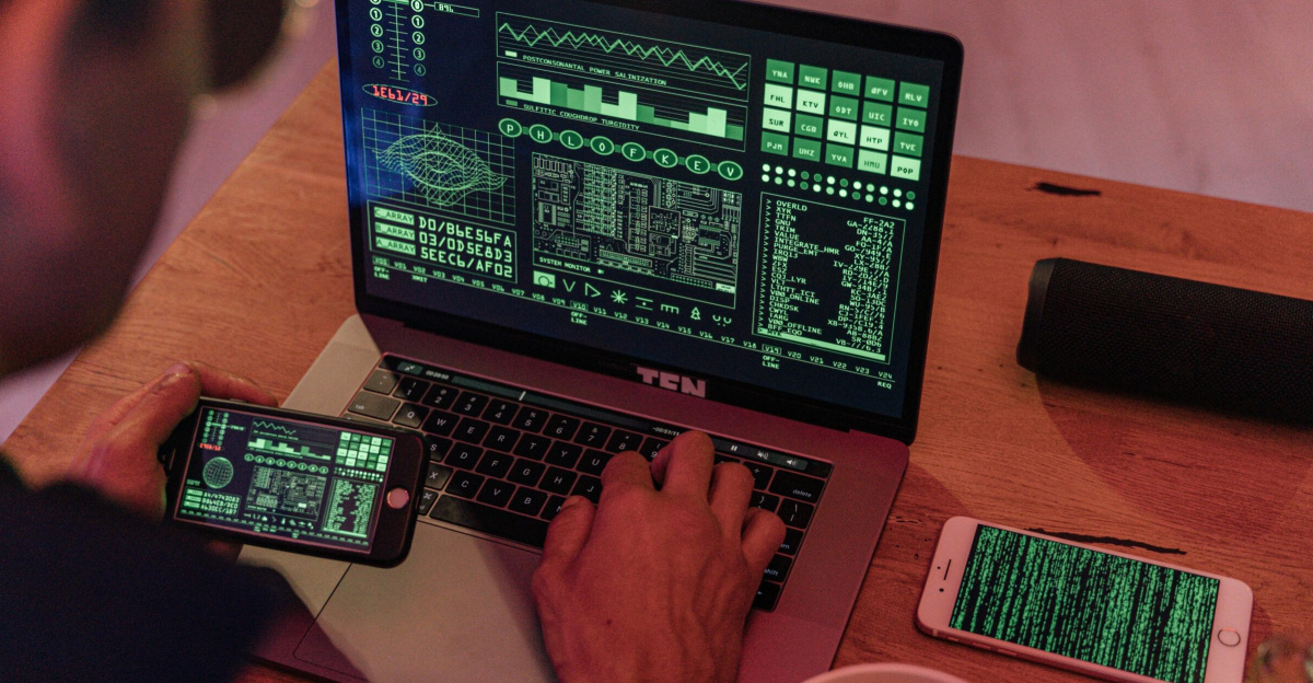 Man working with cybersecurity software on laptop and smartphone.