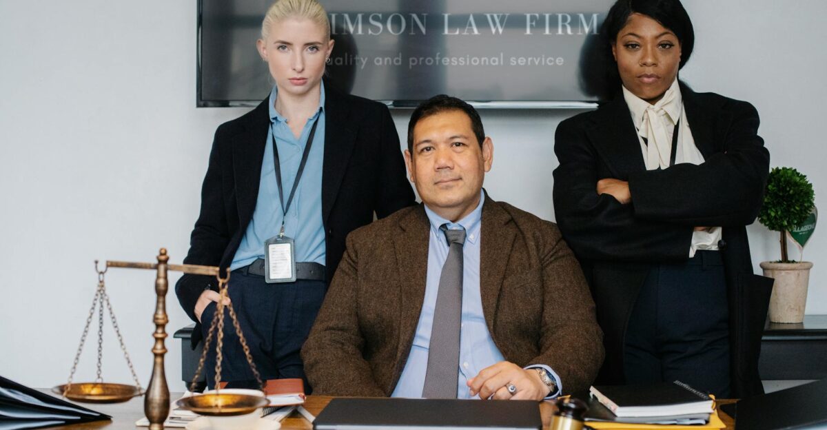 Diverse law firm employees in suits at a desk Scale and gavel signify justice