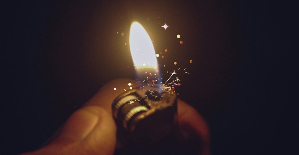 Intense close-up of a lighter igniting a bright flame with spark effects against a dark background
