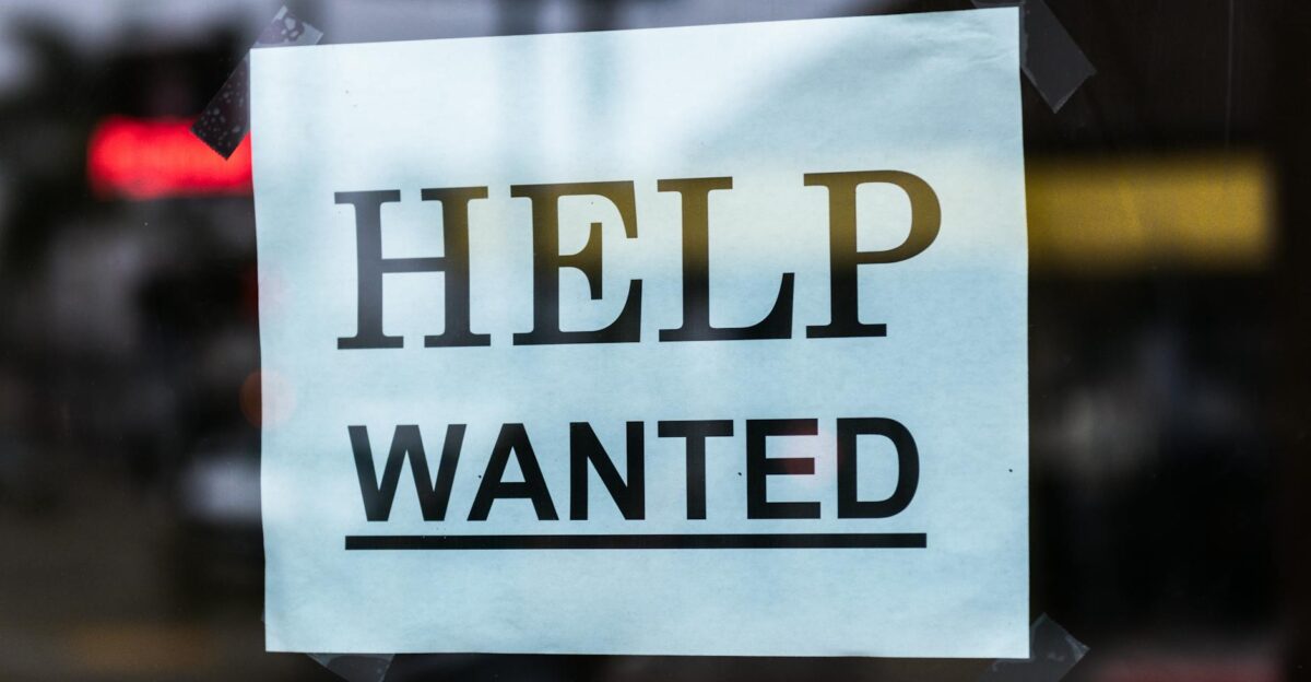 Close-up of a Help Wanted sign taped to a glass window in a storefront