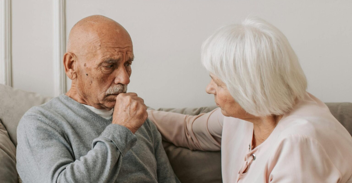 An elderly woman comforts a man coughing on a couch, showcasing care and affection.