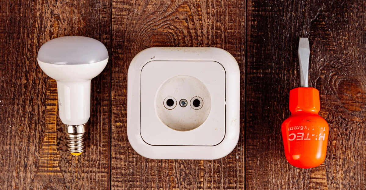Flat lay of a lightbulb, socket, and screwdriver on a rustic wooden surface.
