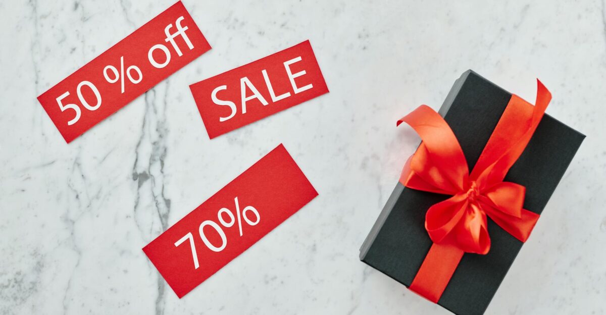 Stylish black gift box with red ribbon and sale tags on marble perfect for Black Friday promotions