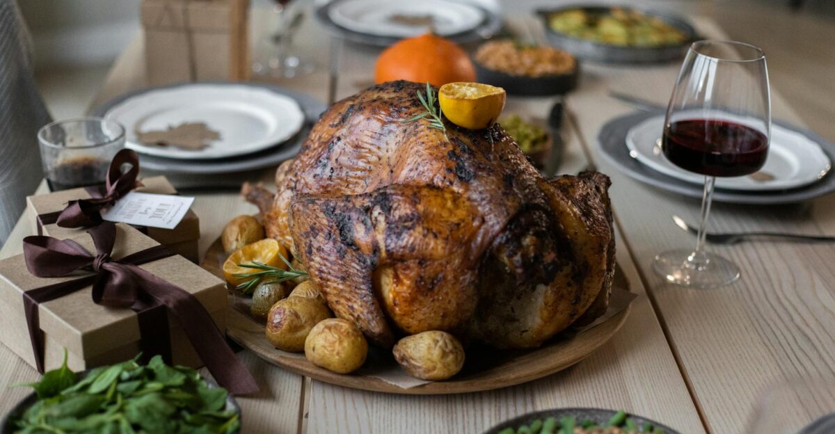 High angle of appetizing roasted turkey and glasses of wine with other dishes placed on wooden table prepared for celebrating Thanksgiving Day