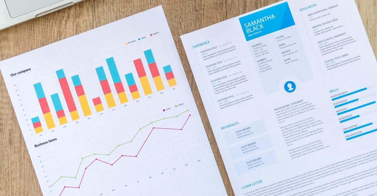 Top view of a laptop, charts, and resume on a wooden desk, showcasing business analysis and job application.