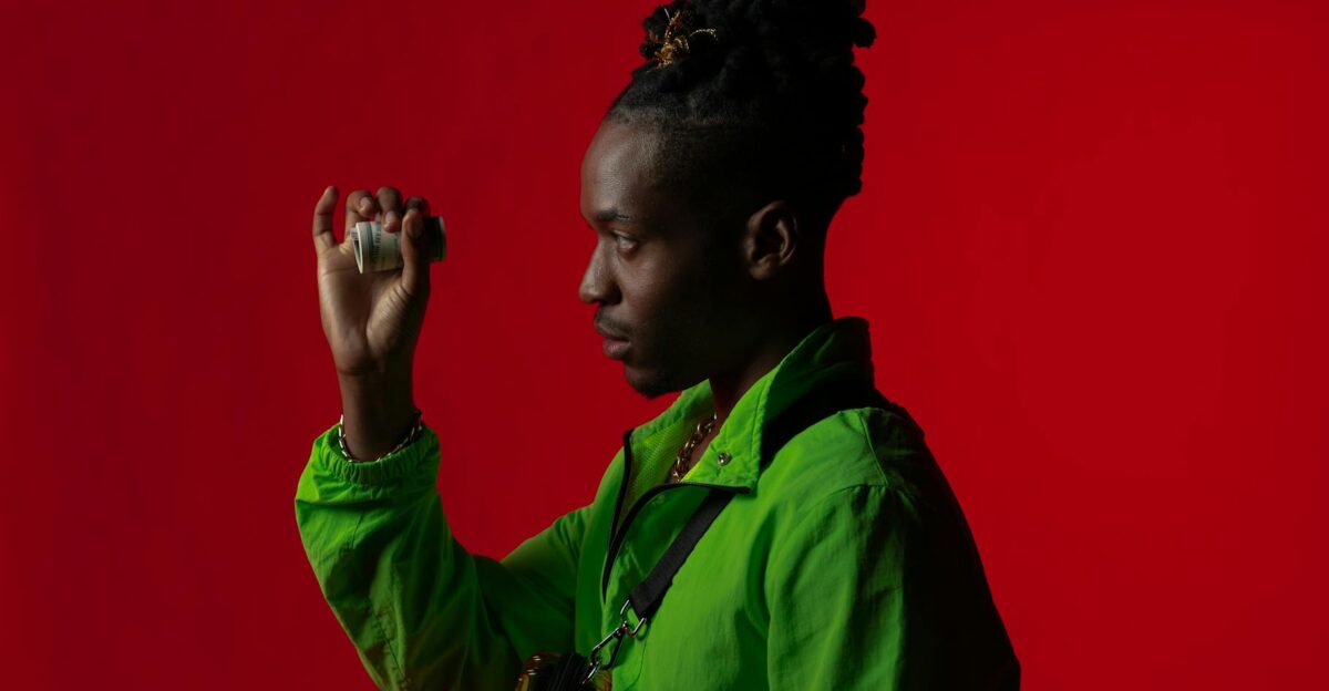Fashionable African American man with dreadlocks holding money against a red backdrop