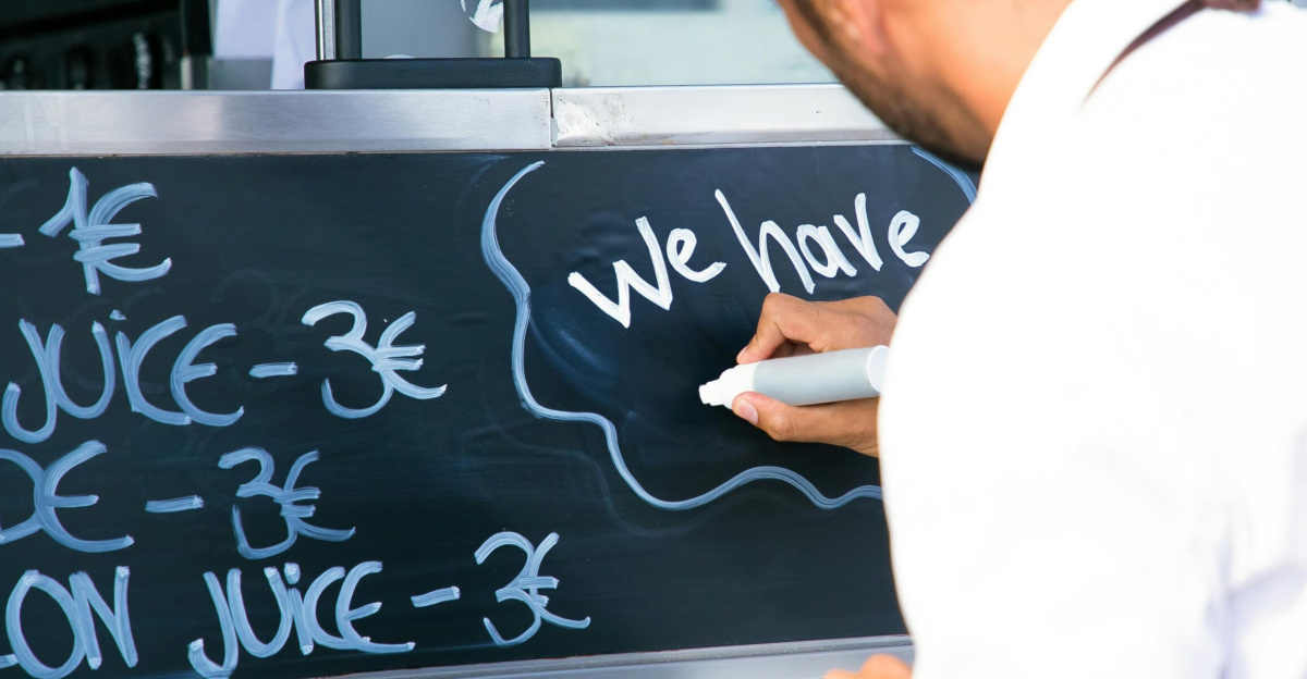 Back view of crop anonymous male worker writing information on marker board for clients of food truck