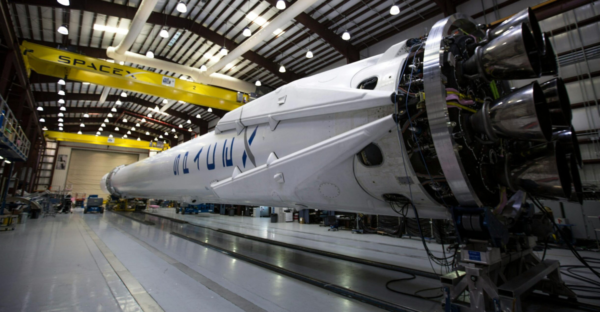 A SpaceX Falcon rocket displayed in a spacious hangar under bright industrial lights.