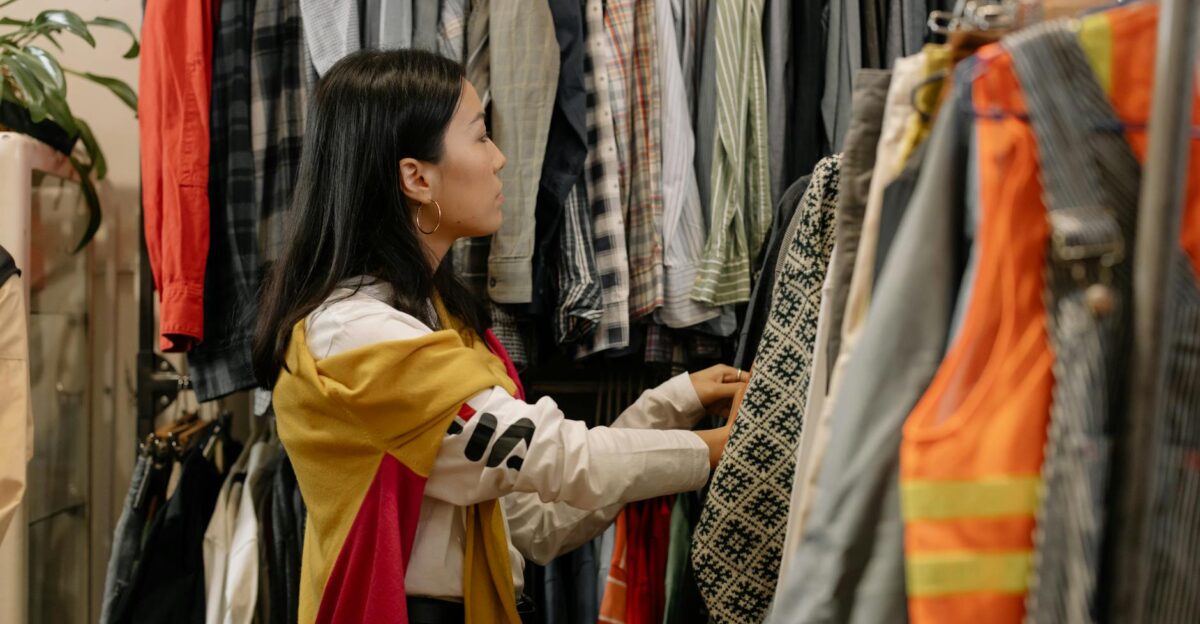 A young woman browsing clothes in a vintage store with colorful outfits