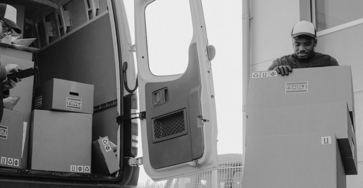 Delivery workers unloading packages from a van using a trolley at a distribution center.