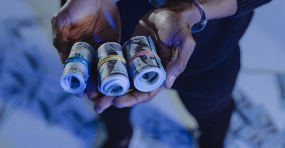 A man in handcuffs holding rolled US dollar bills symbolizing cyber fraud or theft
