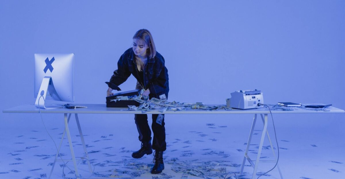 A young woman standing at a desk filled with money suggesting cyber crime or financial scam