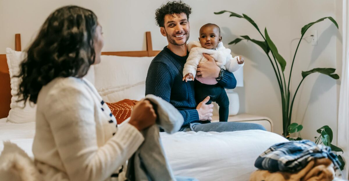 African American mother with clothes and ethnic father with newborn baby looking at each other while spending time in bedroom