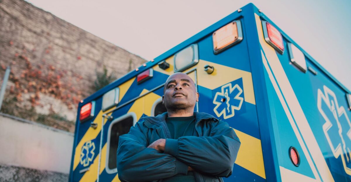 Paramedic stands confidently with arms crossed in front of an ambulance