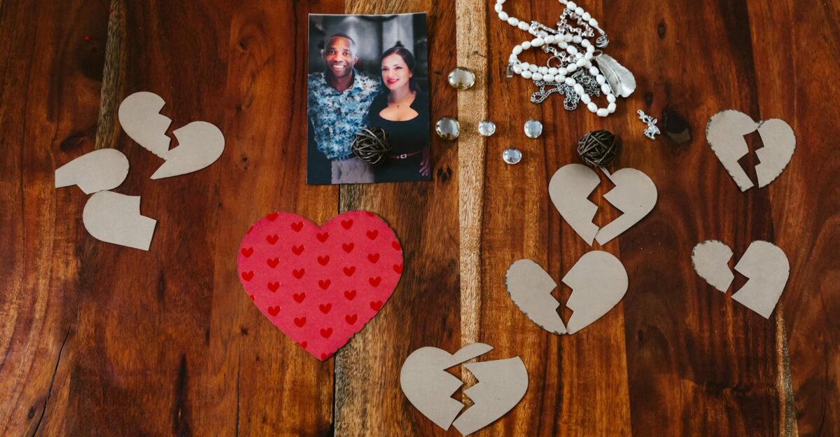 A collection of broken heart symbols jewelry and a couple s photo on a wooden surface