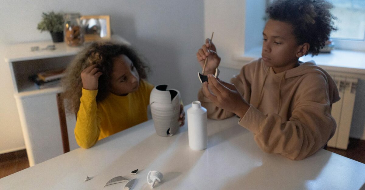 Two children collaborate to fix a broken vase using glue on a table at home