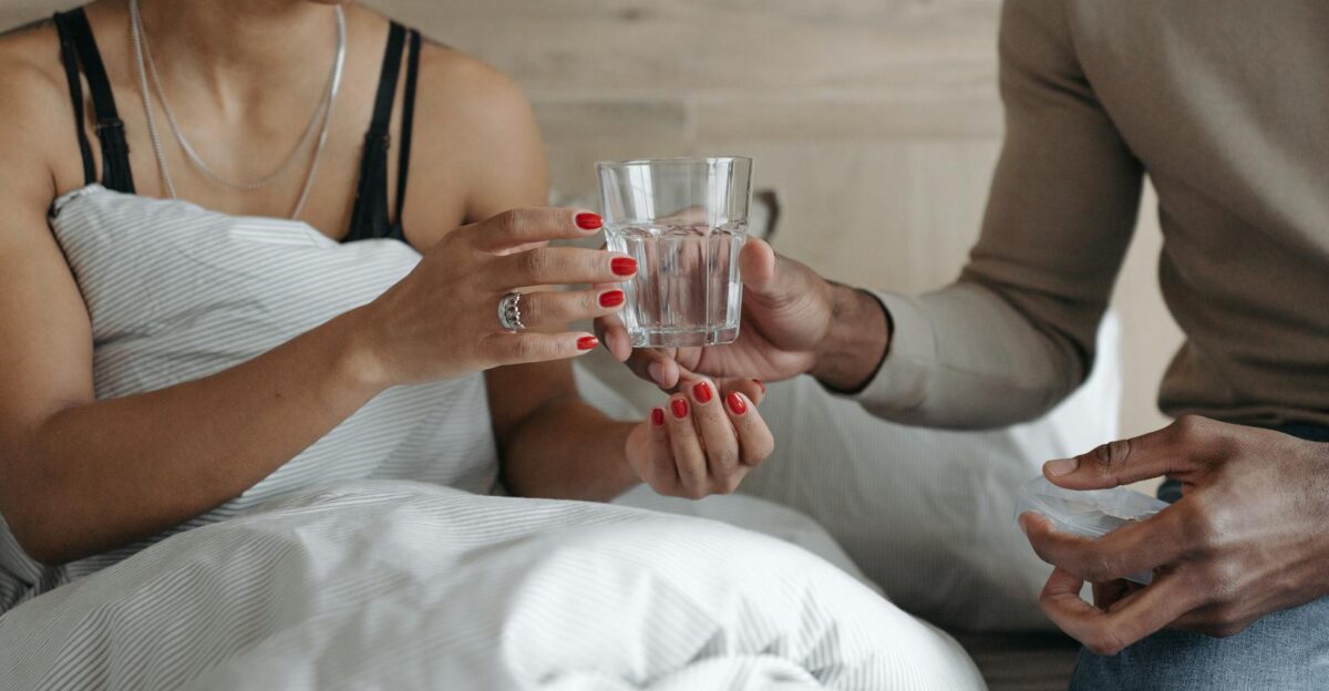 Close-up of a person in bed receiving a glass of water symbolizing care and empathy