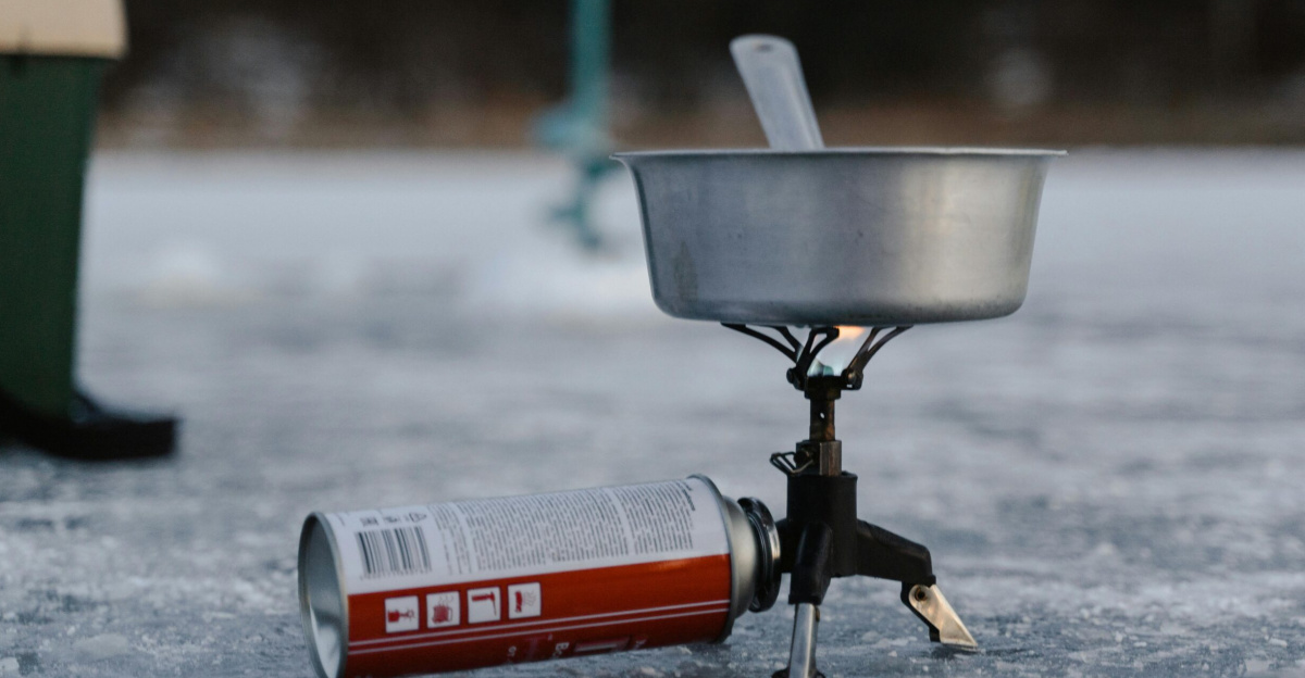 A camping stove setup on ice including a pot and butane canister for winter outdoor cooking.