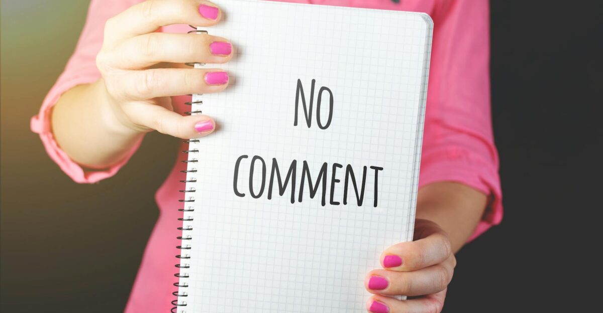 A woman in a pink shirt holds a notebook with No comment text visible conveying silence or privacy