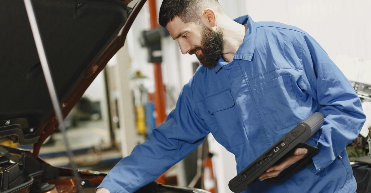 An auto mechanic in blue coveralls inspecting a car s engine in a garage