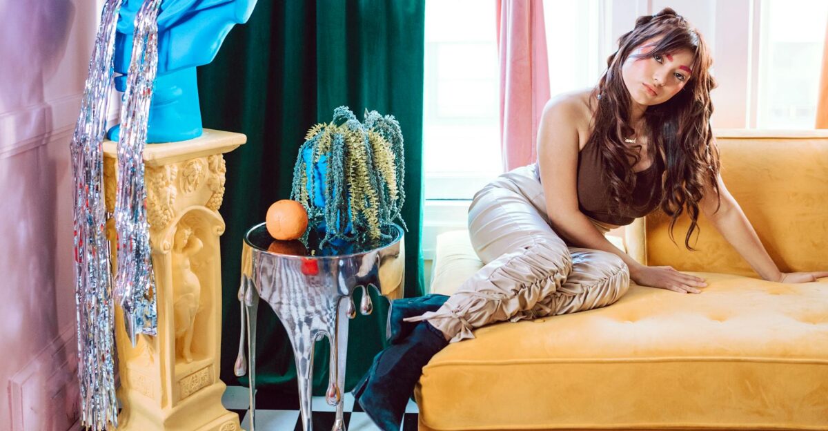 A stylish woman poses in a vibrant living room with colorful decor and modern fashion