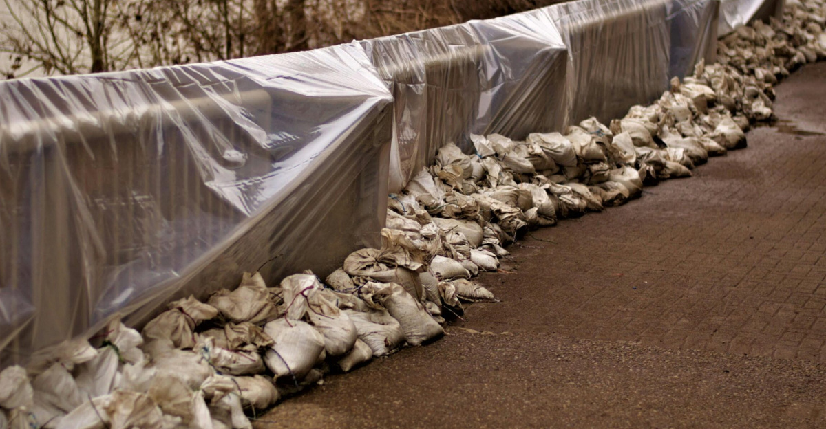An arrangement of sandbags and plastic sheeting for flood protection along a riverside road.