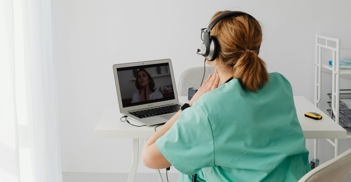 A nurse in a teal uniform conducts a video call consultation from a modern clinic.