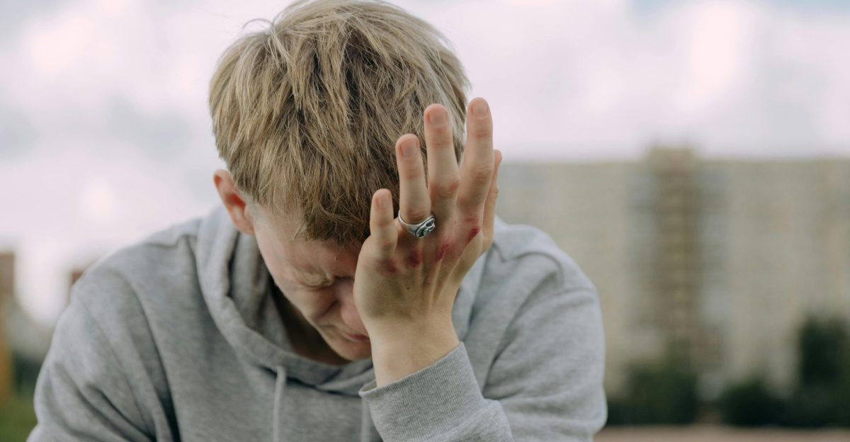 A young man outdoors holding his head in stress, depicting mental health challenges.