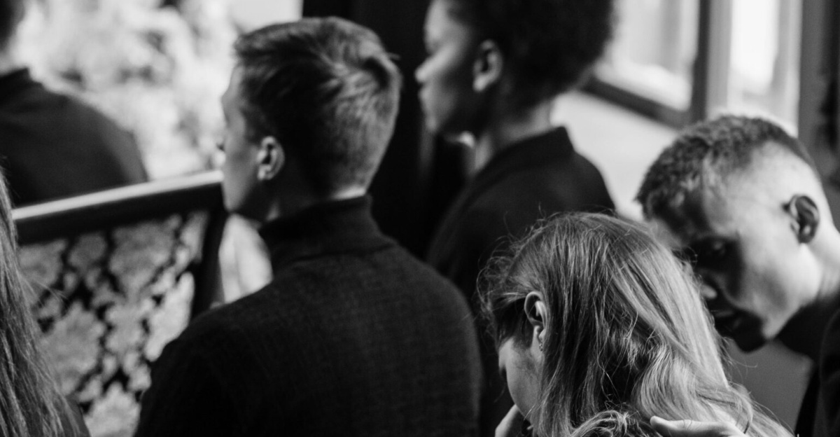 A somber grayscale image of mourners sitting indoors during a funeral, conveying loss and sympathy.