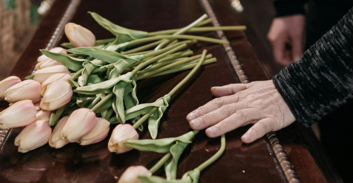 A somber funeral scene with tulips placed on a wooden coffin, symbolizing loss and remembrance.