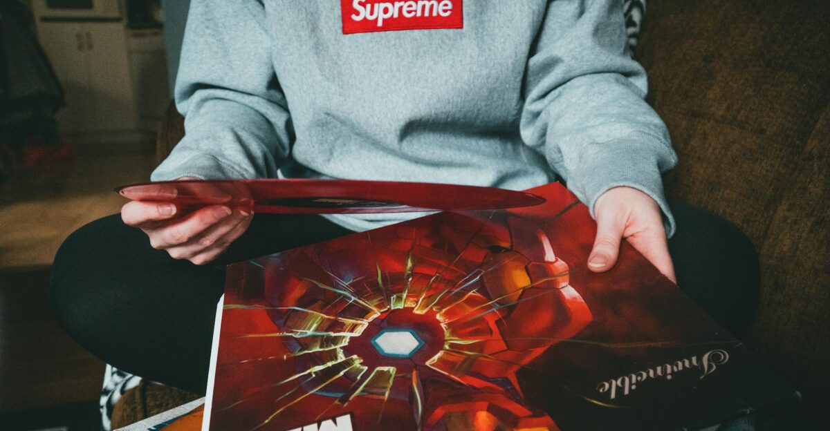 Person in gray hoodie holding Iron Man vinyl record while sitting indoors Trendy and nostalgic vibe