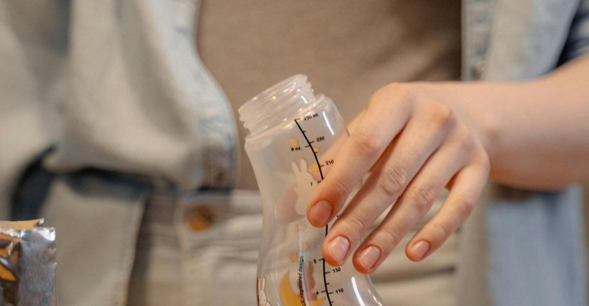 A person preparing a baby bottle with infant formula indoors in a casual setting.