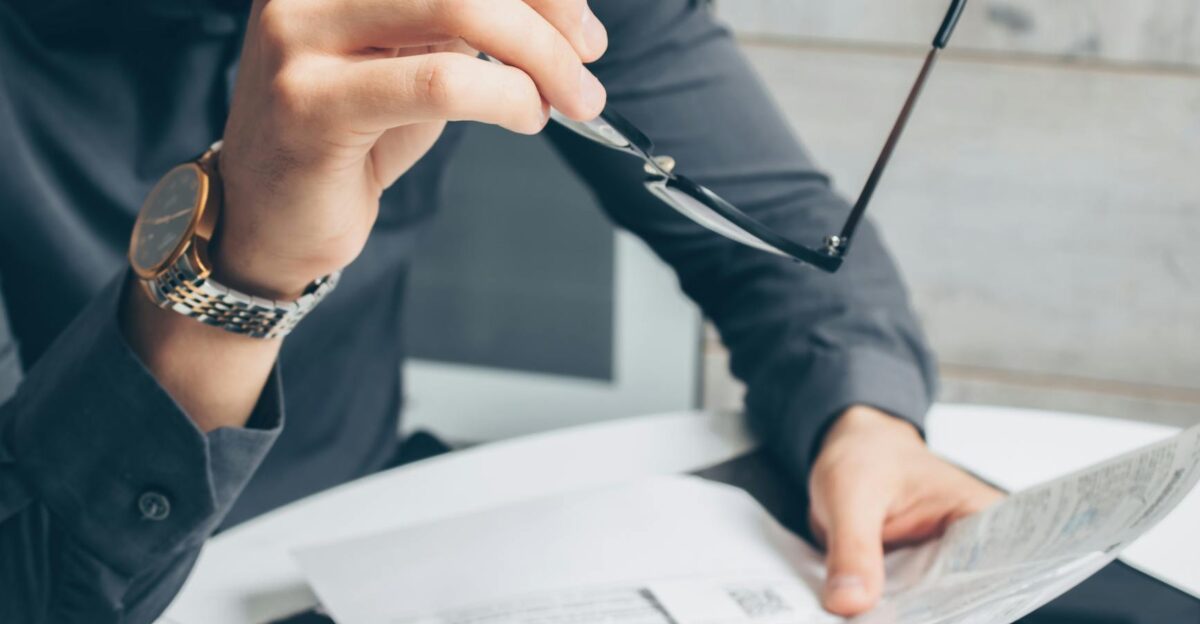 Man in formal attire reviewing paperwork holding glasses Business setting