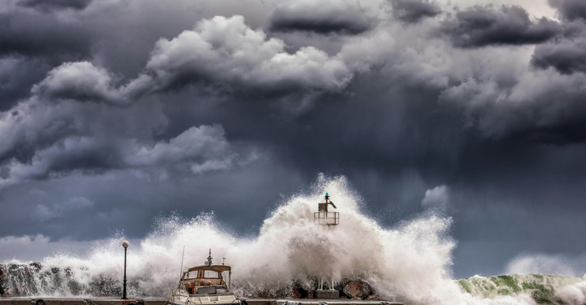 Powerful waves crash against a pier and lighthouse under dark stormy skies.