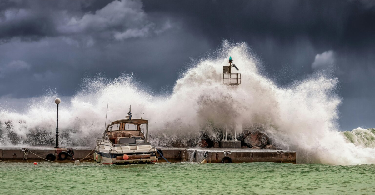 Powerful waves crash against a pier and lighthouse under dark stormy skies.