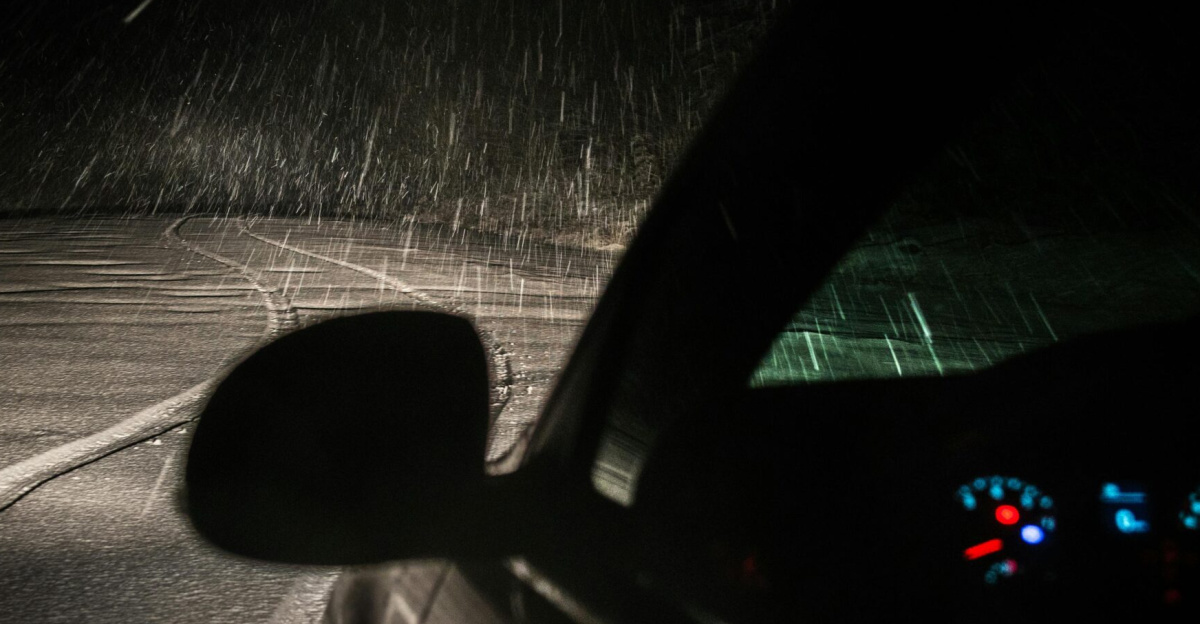 Capture of a car driving through a snowstorm at night, showing snow, road and dashboard lights.